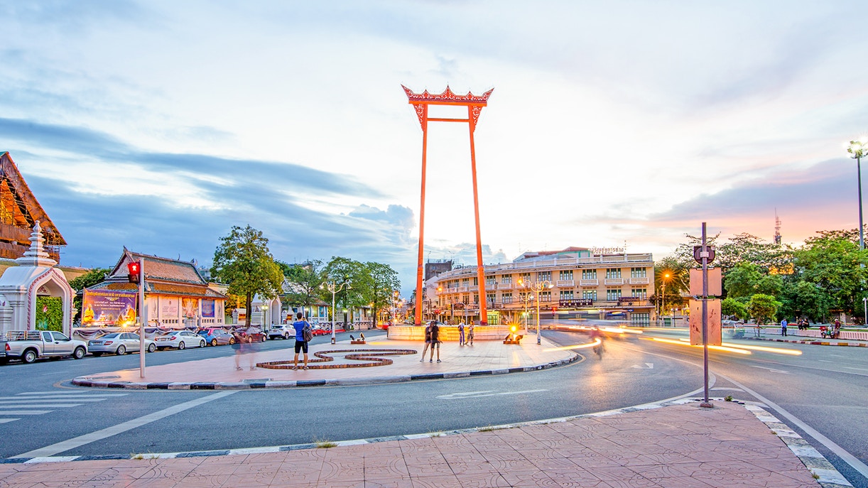 Giant Swing in Bangkok at sunset with people and surrounding buildings.