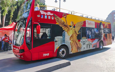 Red double-decker Turibus in Historic Center of Mexico City with iconic landmarks depicted.