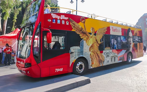 Red double-decker Turibus in Historic Center of Mexico City with iconic landmarks depicted.