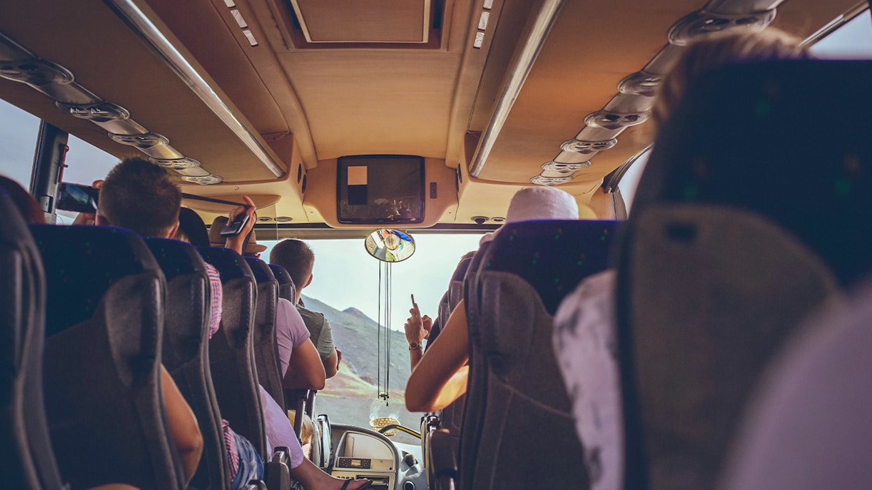 Tourists seated inside a bus, viewing scenic landscape through the front window.
