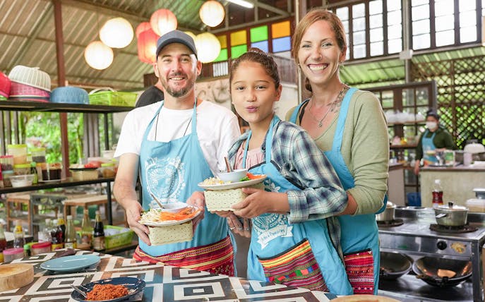 Participants in aprons holding dishes at Thai cooking class in Mama Noi's organic garden.