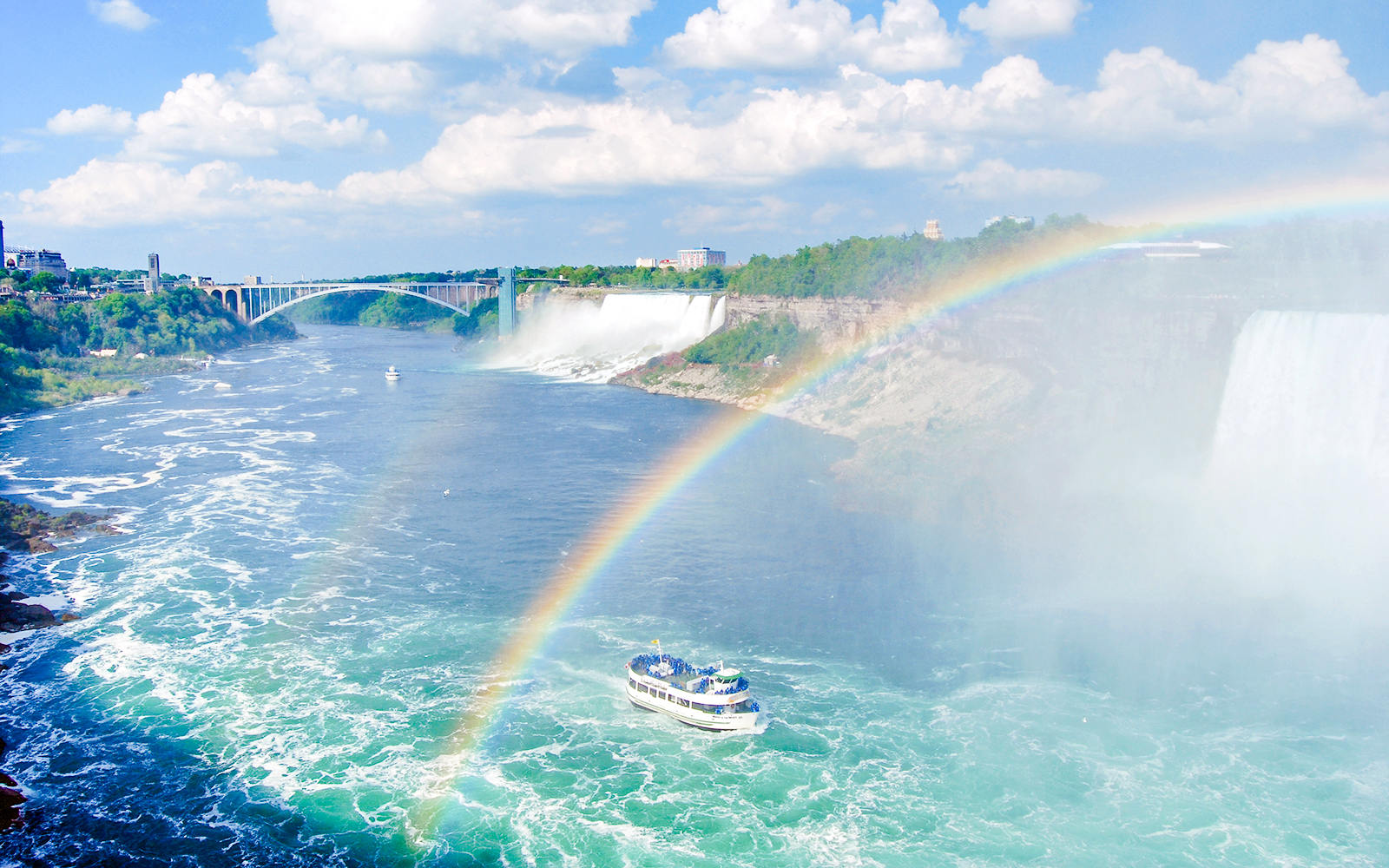 Boat tour approaching Niagara Falls with a rainbow in the mist, USA.