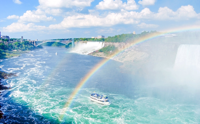 Boat tour approaching Niagara Falls with a rainbow in the mist, USA.