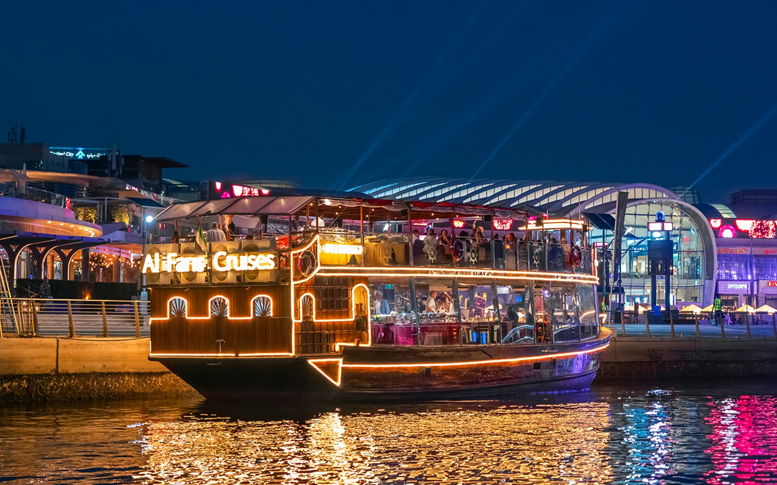 Dhow cruise on Dubai Canal with city skyline and illuminated bridge.