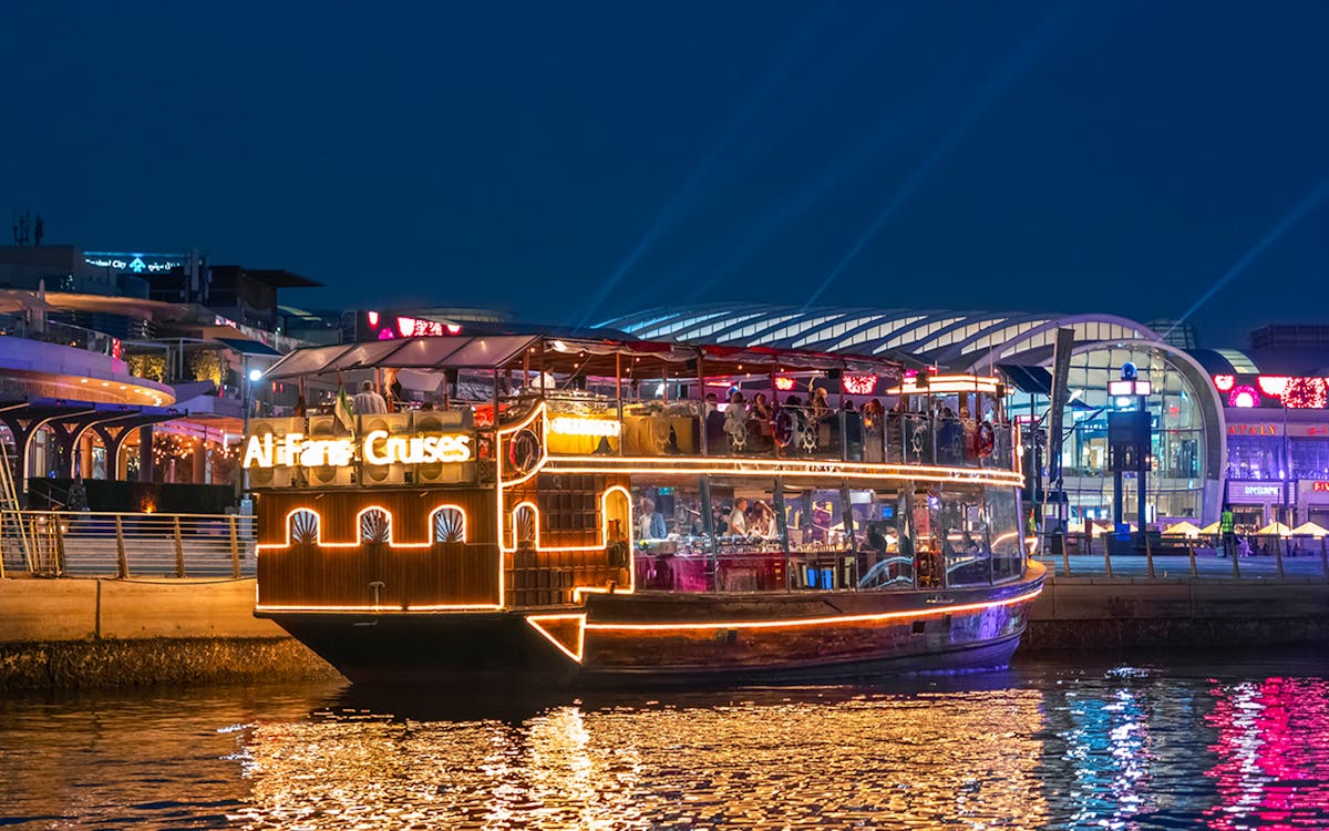 Dhow cruise on Dubai Canal with city skyline and illuminated bridge.