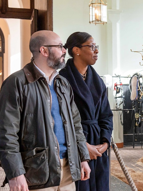 Visitors observing a white horse in harness at the Royal Mews stables.