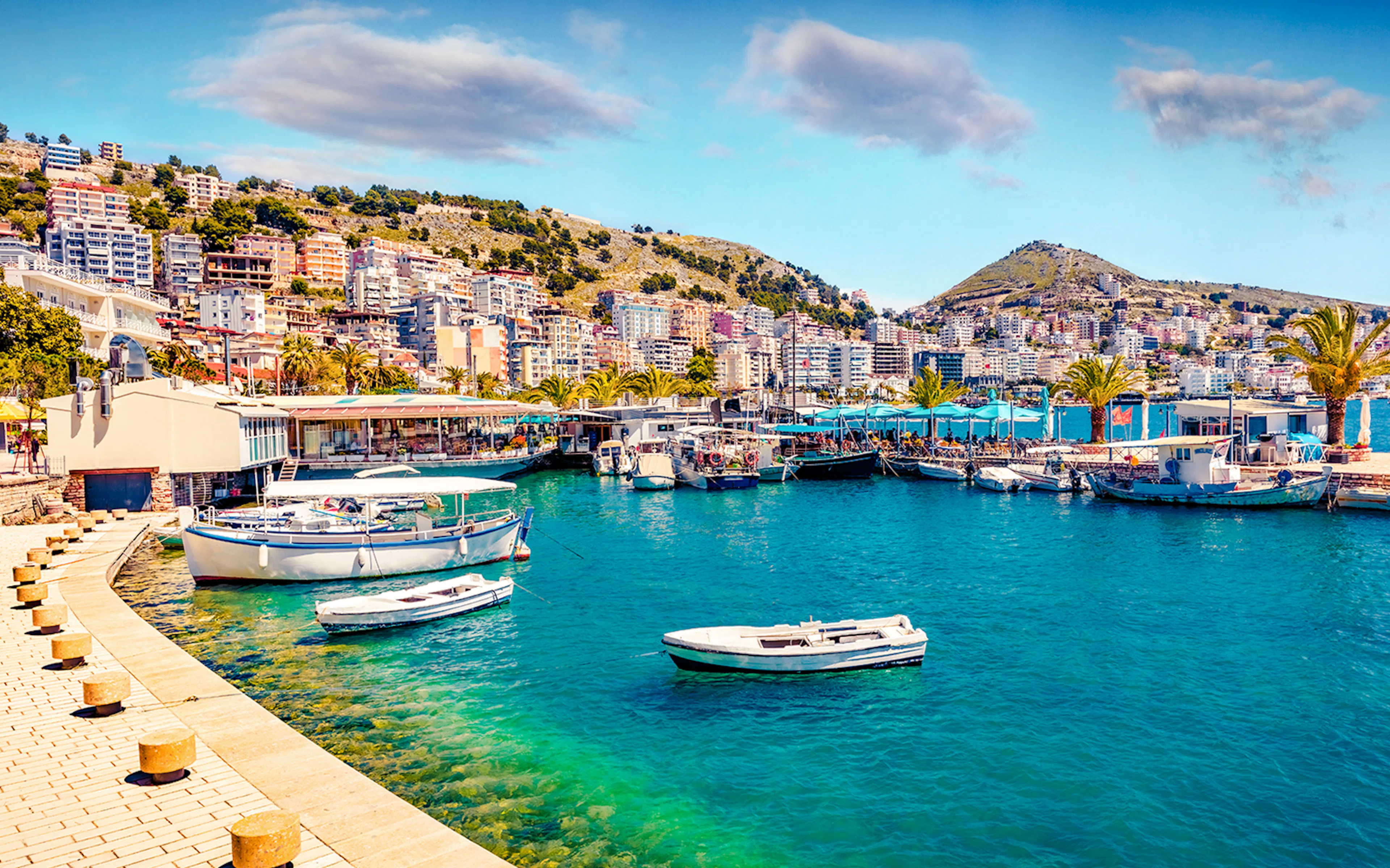 Saranda port cityscape with boats and hillside buildings in spring.