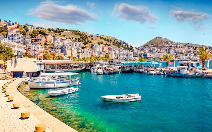 Saranda port cityscape with boats and hillside buildings in spring.