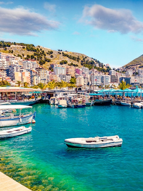 Saranda port cityscape with boats and hillside buildings in spring.