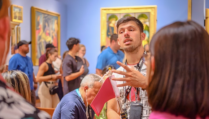 Guide explaining artwork to tourists at Accademia Gallery, Florence.
