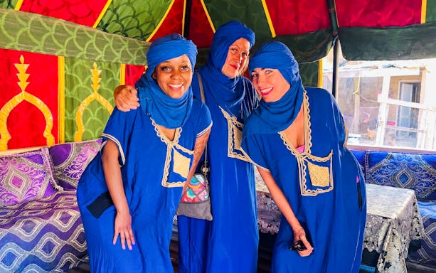 Visitors in traditional Moroccan attire inside a colorful tent during Palmeraie camel ride tour.