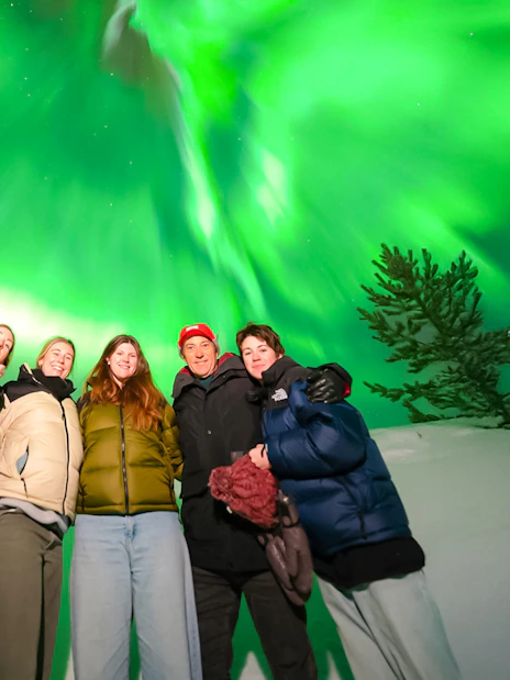 Guests on Northern Lights Chase Bus Tour in Rovaniemi under vibrant aurora borealis.