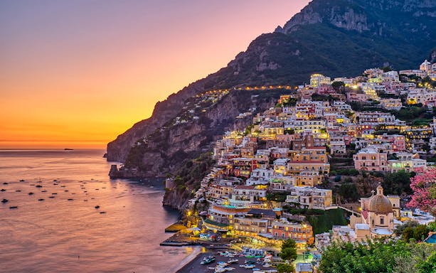 Sorrento hills at sunset with colorful buildings and boats on the coast.