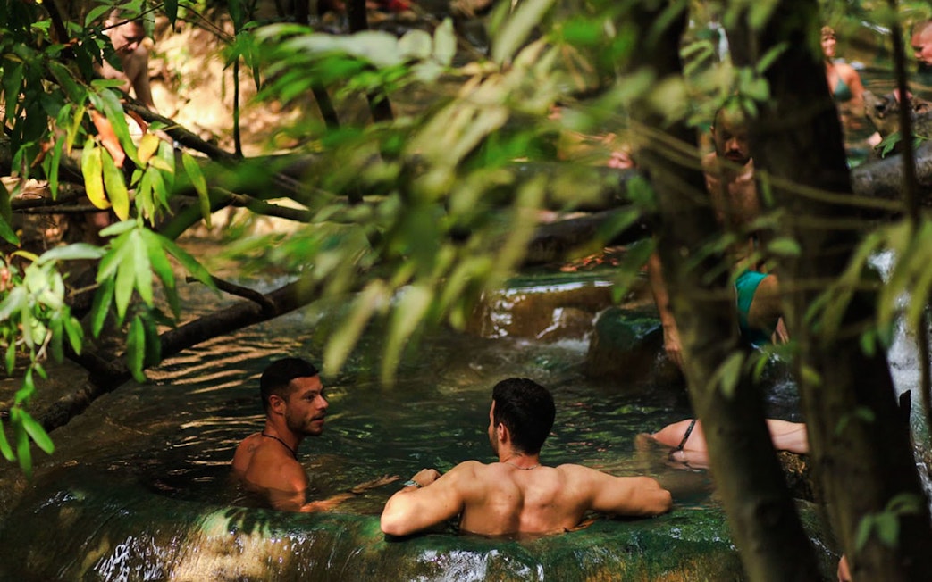 Tourists relaxing in the emerald pool surrounded by lush greenery in Krabi, Thailand.