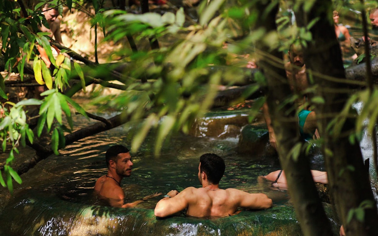 Tourists relaxing in the emerald pool surrounded by lush greenery in Krabi, Thailand.