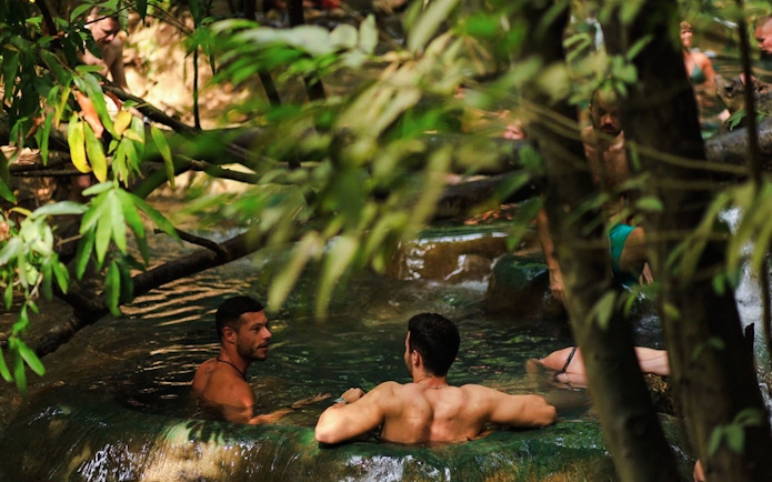Tourists relaxing in the emerald pool surrounded by lush greenery in Krabi, Thailand.