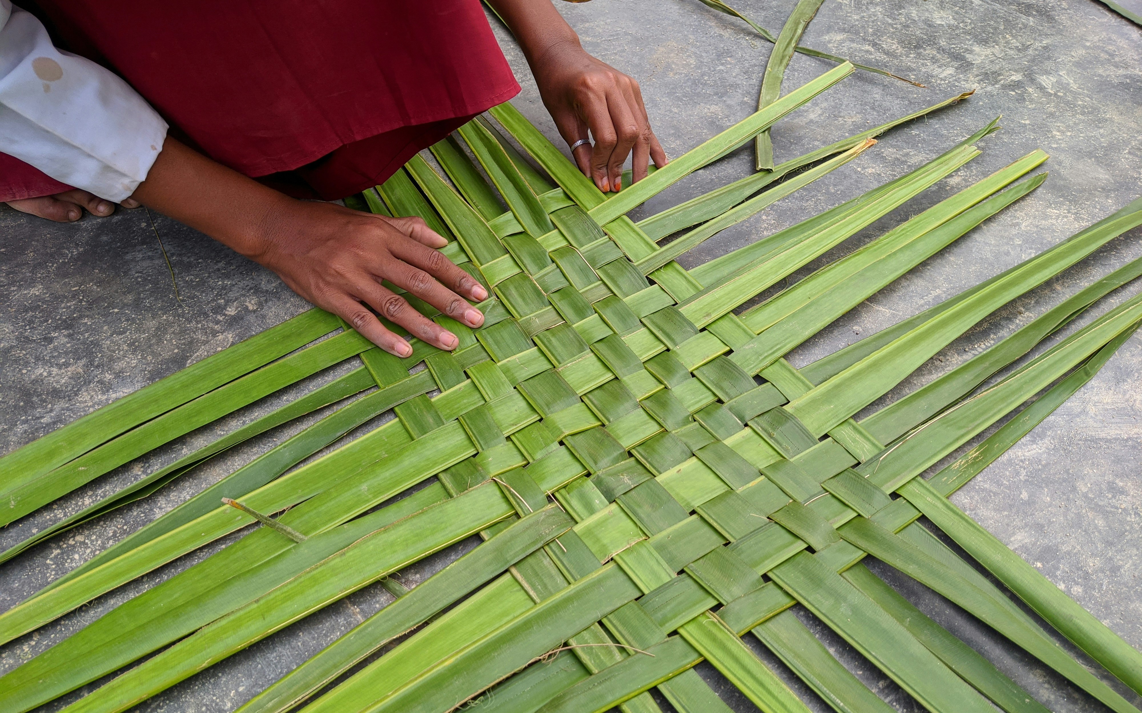 Weaving coconut palm leaves by hand on a stone surface.