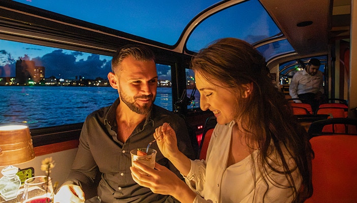 Couple enjoying dessert on an Amsterdam dinner cruise with city skyline in the background.
