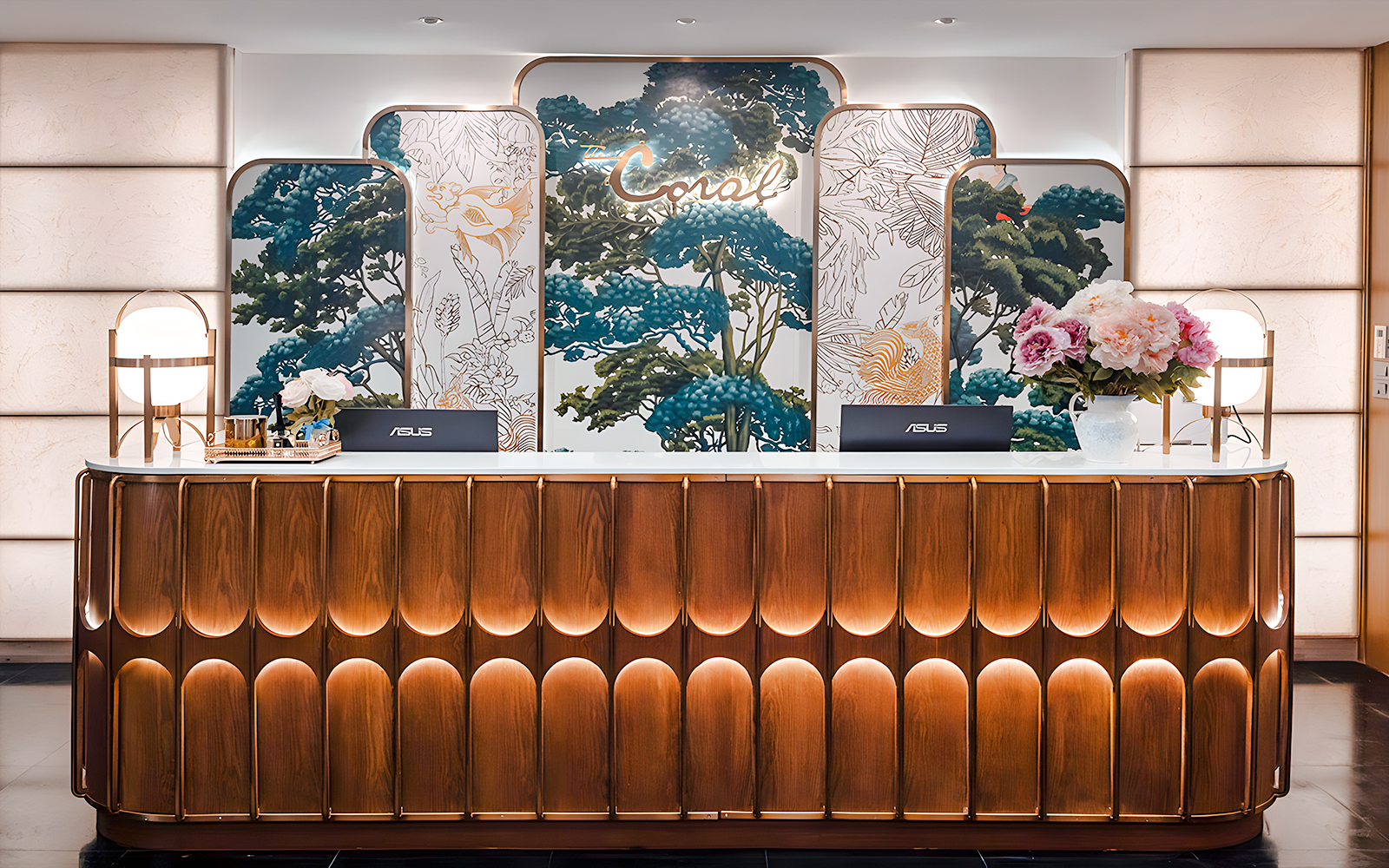 Reception desk at The Coral First Class Lounge, Bangkok airport, featuring floral decor and elegant lighting.