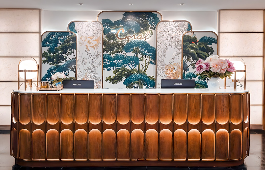 Reception desk at The Coral First Class Lounge, Bangkok airport, featuring floral decor and elegant lighting.