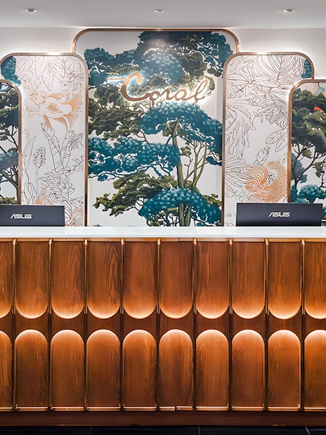 Reception desk at The Coral First Class Lounge, Bangkok airport, featuring floral decor and elegant lighting.