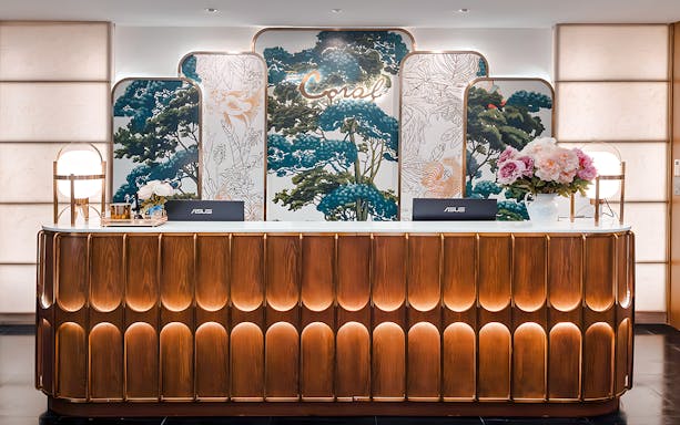 Reception desk at The Coral First Class Lounge, Bangkok airport, featuring floral decor and elegant lighting.
