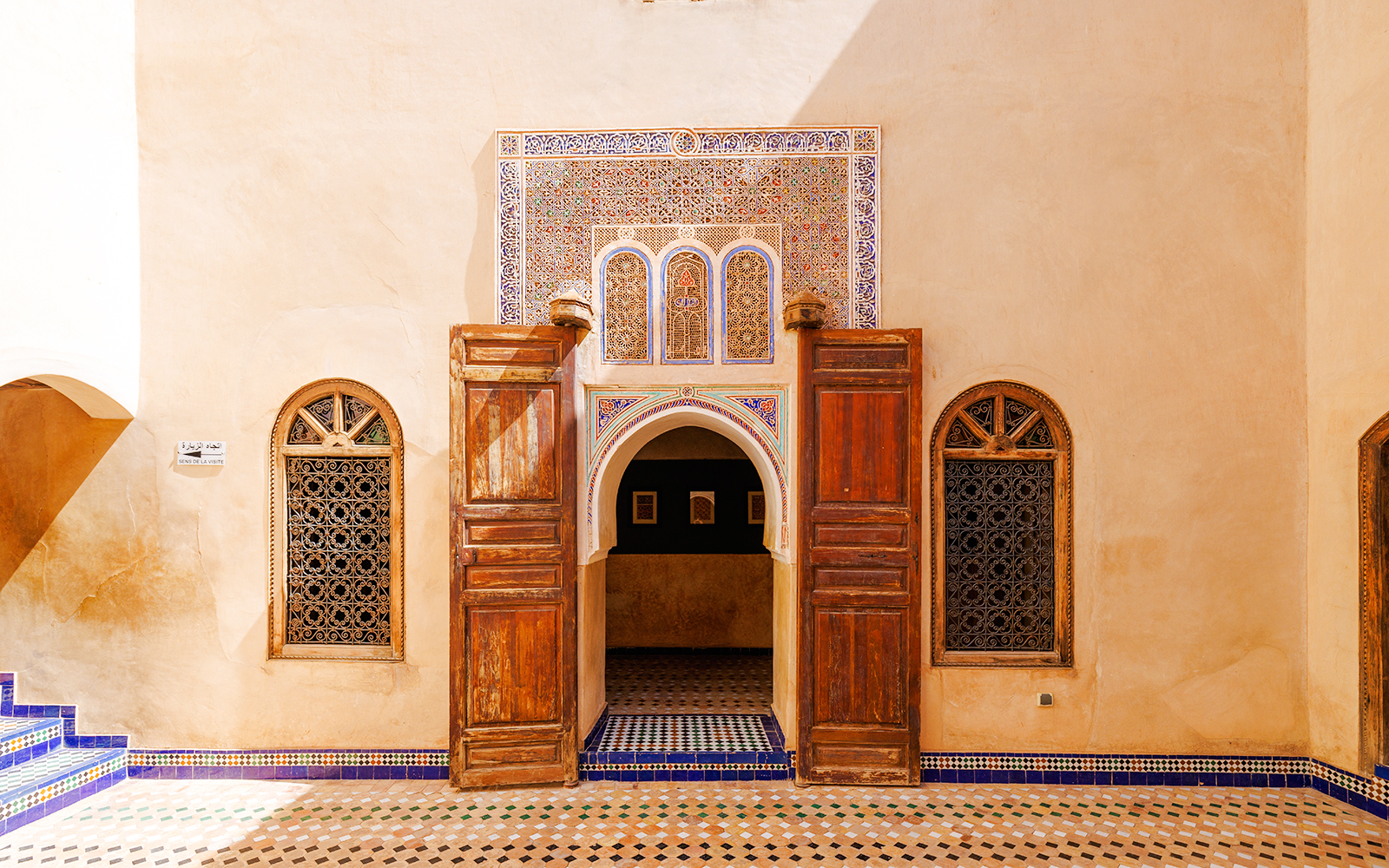 Ornate entrance with wooden doors and mosaic tiles at Bahia Palace, Marrakech, Morocco.