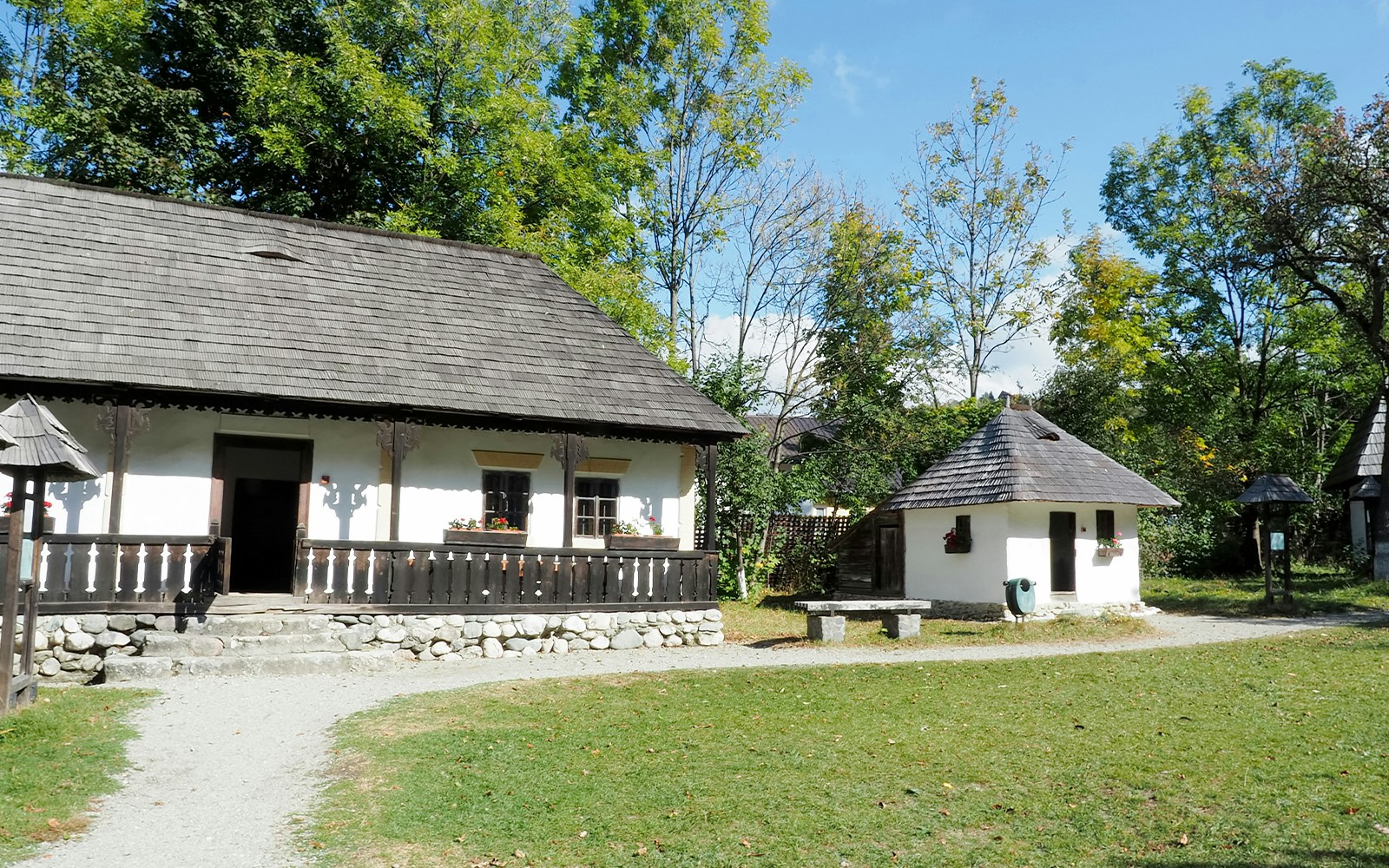 Traditional houses in Bran Village Museum, Romania, surrounded by trees and a grassy area.
