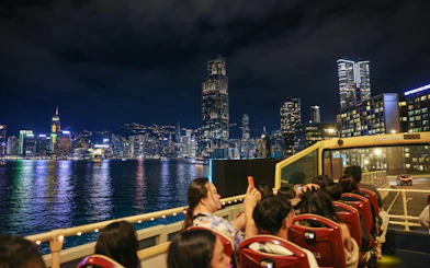 Open-top bus tour with passengers viewing Hong Kong skyline at night.