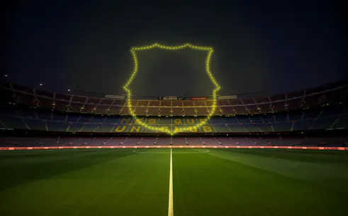 Camp Nou stadium with luminous drone show outline and "Més que un club" slogan.