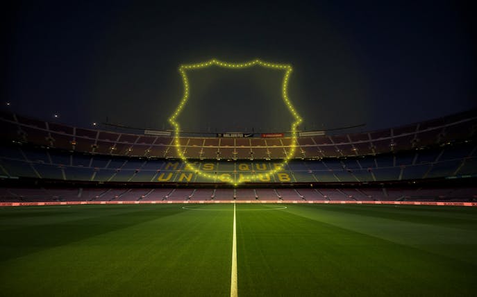 Camp Nou stadium with luminous drone show outline and "Més que un club" slogan.