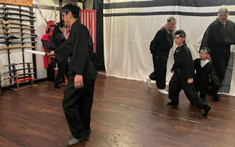 Participants practicing ninja skills at an Osaka Ninja Workshop, surrounded by traditional swords.
