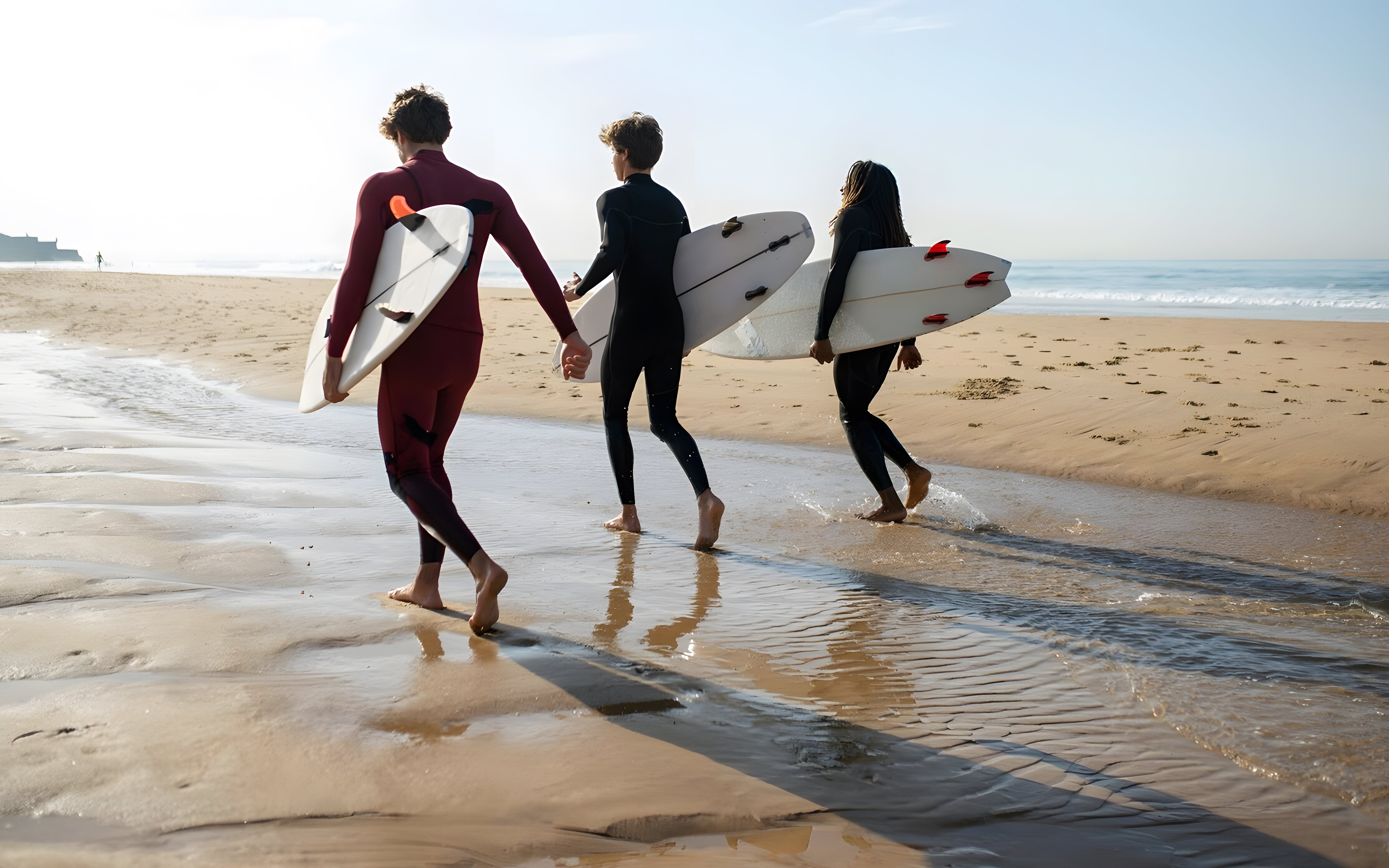 Tourists with surfboards walking on a beach after a surf class in Lisbon.
