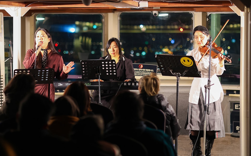 Live music performance on Eland Cruise, Seoul, featuring a singer, keyboardist, and violinist.