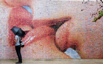 Person with umbrella viewing The Kiss Mural in Barcelona's Gothic Quarter.