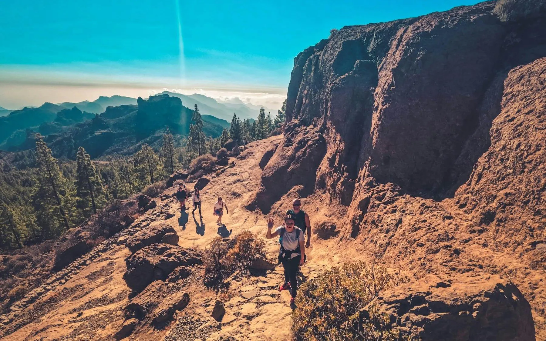 Hikers on a rocky trail with volcanic landscape in Gran Canaria during sunset.