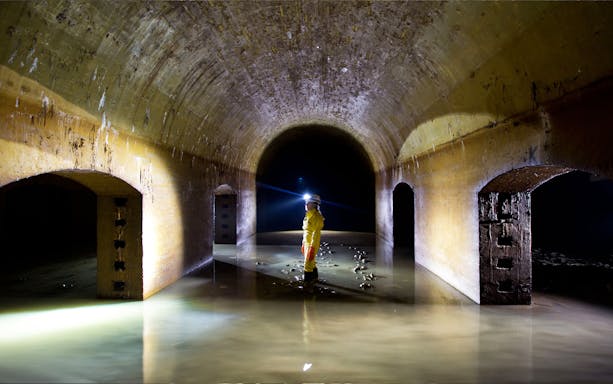 Person exploring underground tunnel in Ancona with headlamp illuminating the passage.