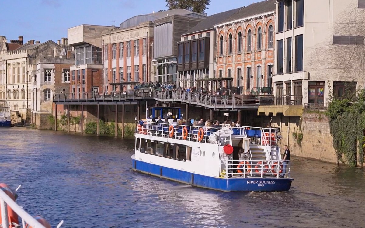 River cruise boat on the River Ouse passing historic buildings in York.