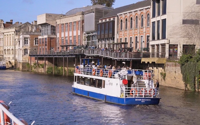 River cruise boat on the River Ouse passing historic buildings in York.