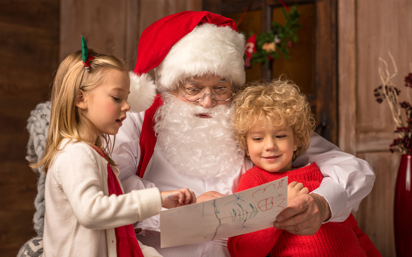 Santa Claus reading a letter with two children during a holiday event.