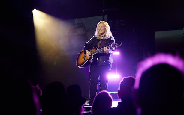 Musician performing on stage with guitar under spotlight during "Melissa Etheridge: My Window" event.