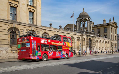 Red double-decker bus on Oxford street near historic building, part of 24/48-Hr Hop-On Hop-Off Tour.