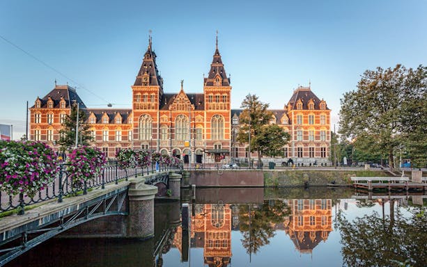 Rijksmuseum exterior with canal reflection and bridge in Amsterdam.