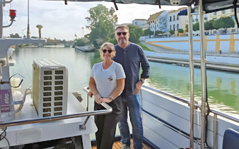 Couple enjoying Seville Guadalquivir River sightseeing cruise with cityscape view.