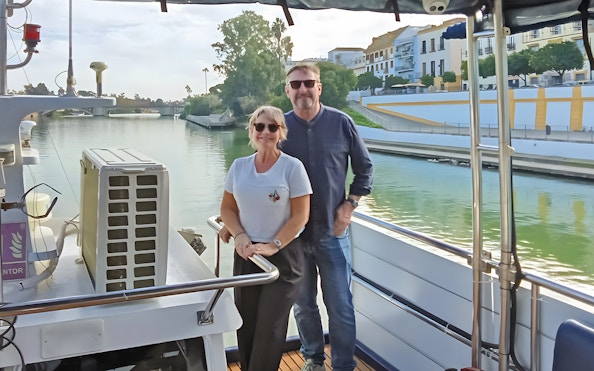 Couple enjoying Seville Guadalquivir River sightseeing cruise with cityscape view.