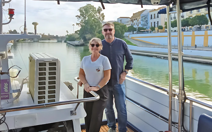 Couple enjoying Seville Guadalquivir River sightseeing cruise with cityscape view.