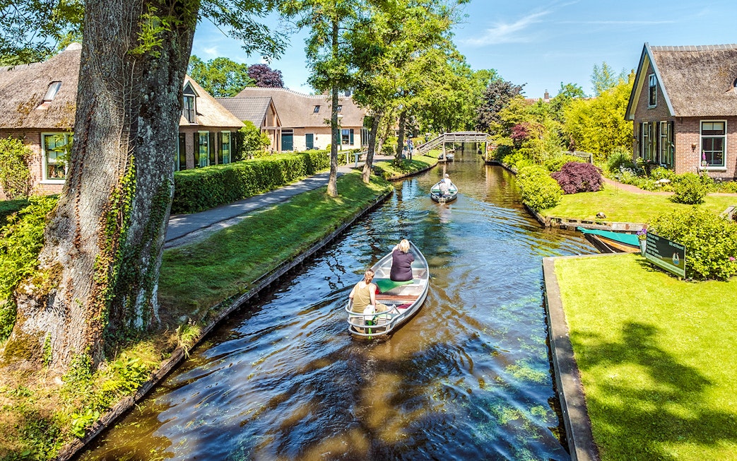 Small electric boat tour through Giethoorn canal with traditional houses and bridge.