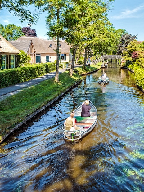Small electric boat tour through Giethoorn canal with traditional houses and bridge.
