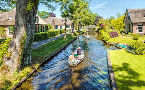 Small electric boat tour through Giethoorn canal with traditional houses and bridge.