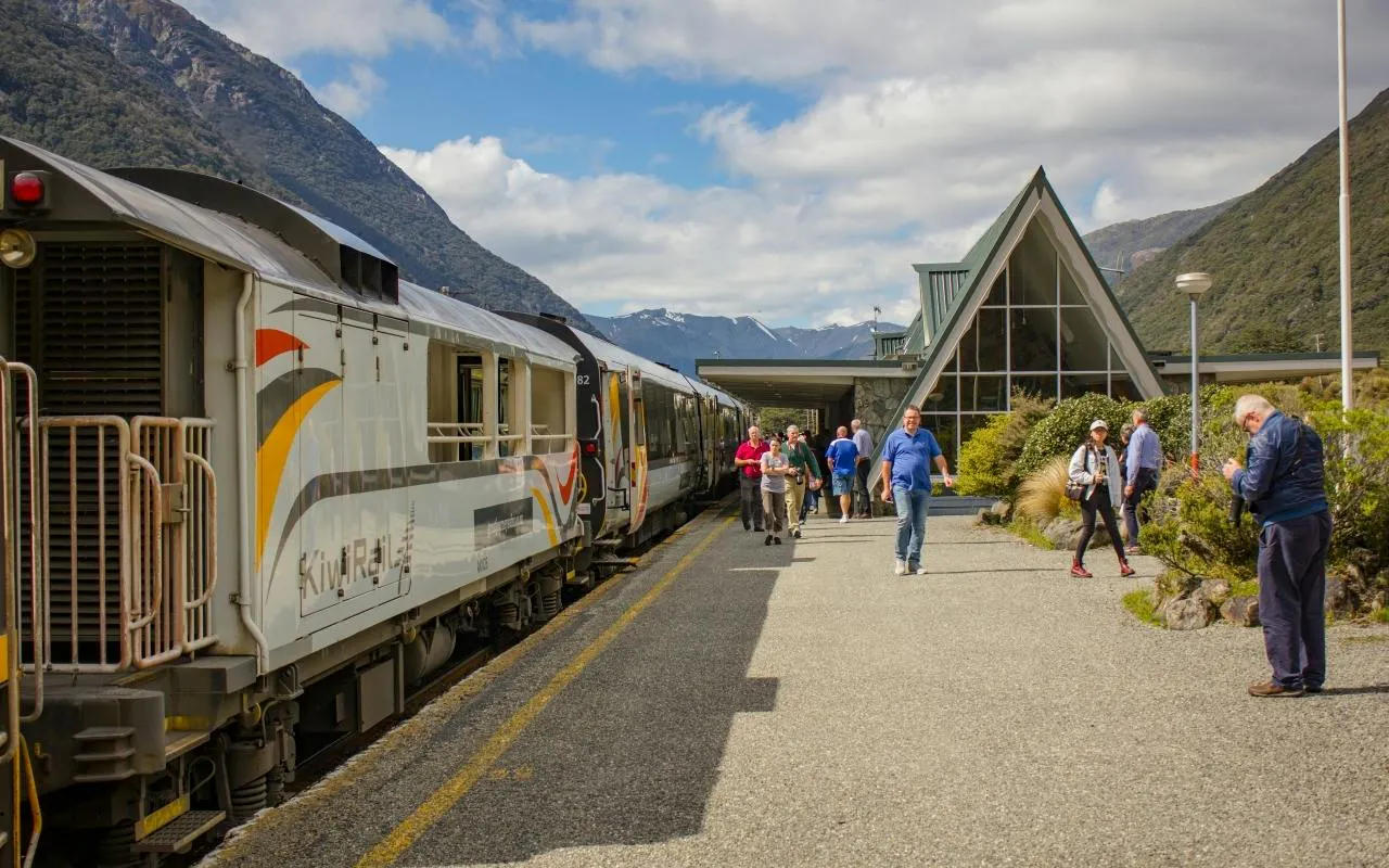 TranzAlpine train at Arthur’s Pass station with passengers, mountains in background, Christchurch tour.